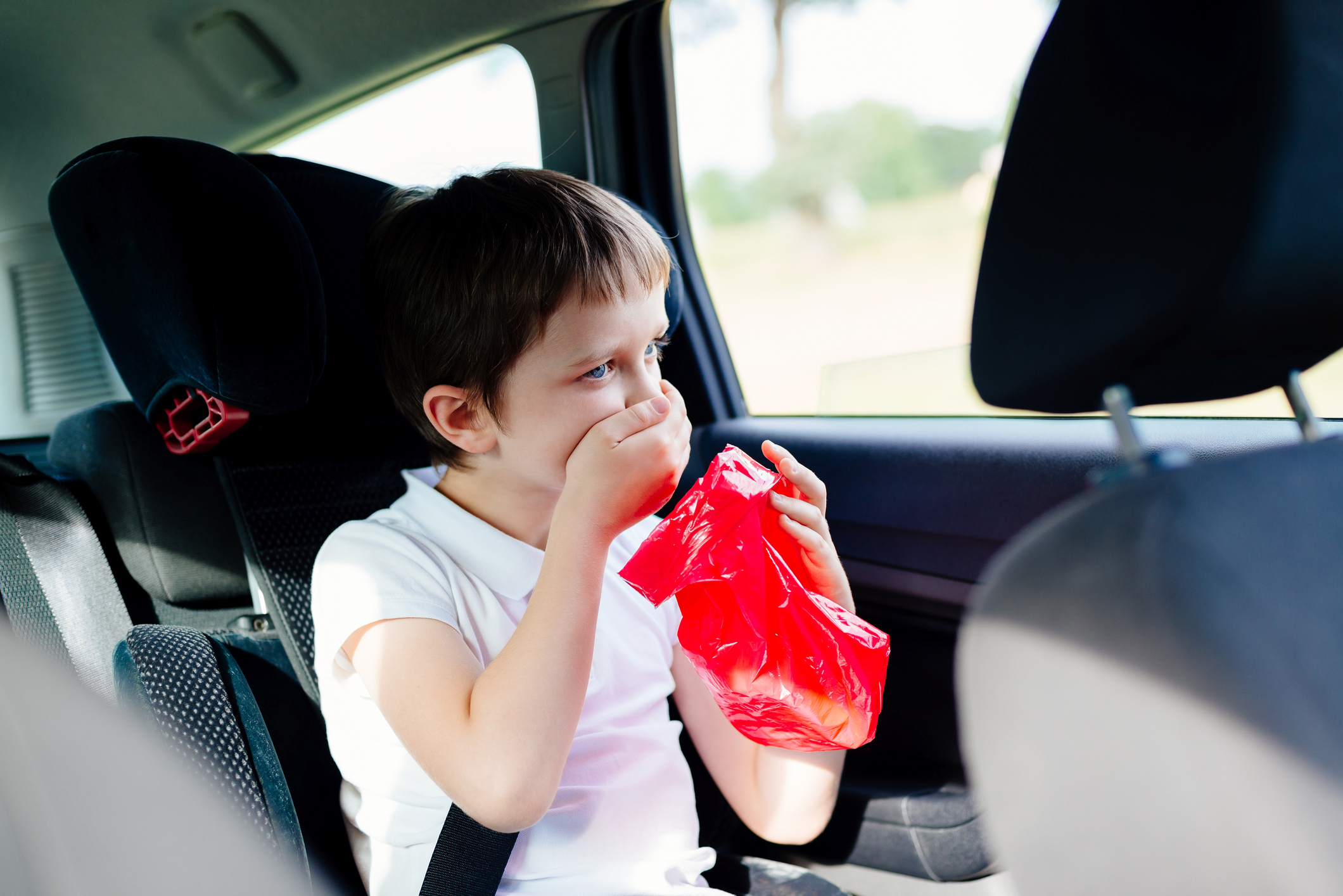 Chlapec v autě držící kapsu na zvracení a ústa. Je mu špatně, pocit na zvracení, tíha, kinetóza